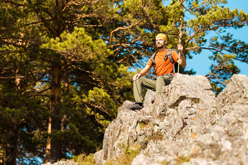 Young male with beard is traveling through the mountain, tourist rucksack standing on rock hill while enjoying nature view, summer holidays in mountains
