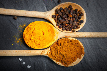 spices in wooden spoons over black stone background, top view
