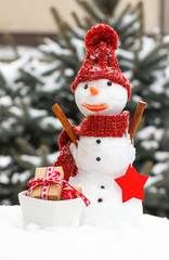 Decorated snowman with gifts for Christmas or Valentine on background of coniferous tree covered snow