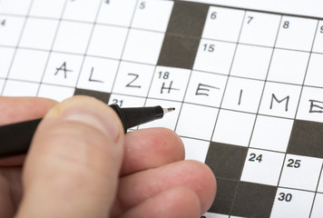 A person is doing a crossword puzzle. The word alzheimer is written on it. Good training for brains for elderly people and stress relieve. Focus point on the pen tip.