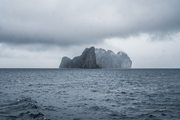 Boat trip to tropical islands. View on beautiful big rock on the sea during cloudy rainy day