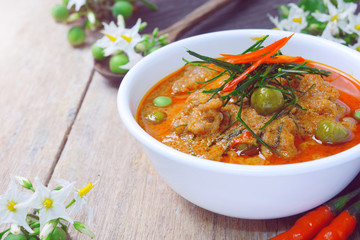 thai red curry fried with pork and coconut milk (panaeng) on white bowl with rice decorated by turkey berry and flower on wooden table.