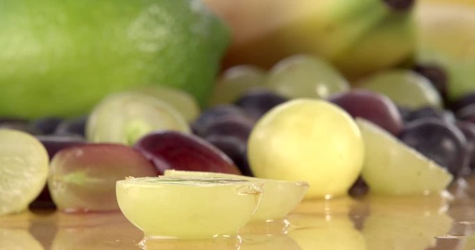 Slicing a grape in half using a sharp kitchen knife. Filmed with selection of fruit in background and on a wooden chopping board. Filmed in slow motion.