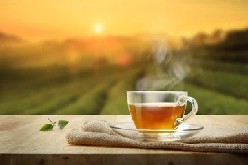 Wall murals Tea Cup of hot tea and tea leaf on the wooden table and the tea plantations background