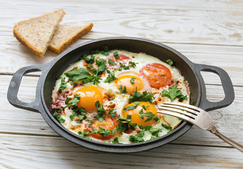 Pan of fried eggs, tomatoes and parsley with bread