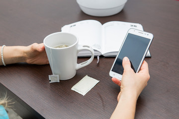 ragazza con tazza, cellulare e agenda sul tavolo