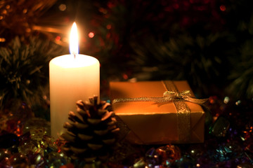 Christmas and New Year`s  evening burning candle and  present gift box wrapped in paper with bows of gold ribbons. Retro style greeting card yellow toned background with holiday tinsel and fir cone.