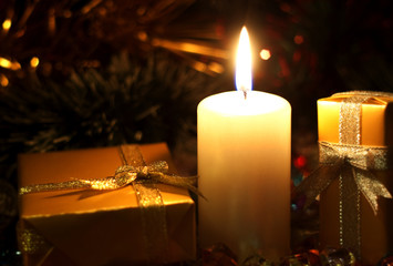 Christmas and New Year`s  evening burning candle and  gold present boxes wrapped in  paper with bows of gold and silver ribbons. Retro style greeting card yellow toned background with holiday tinsel.