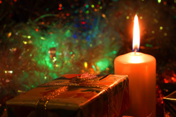 Christmas and New Year`s evening burning candle and present box wrapped in colorful wrapping paper with bows of gold ribbons. Retro style greeting card yellow toned background with holiday tinsel.