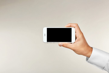 Man's hand holding smartphone on light background