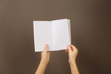Female hands holding blank open brochure on grey background