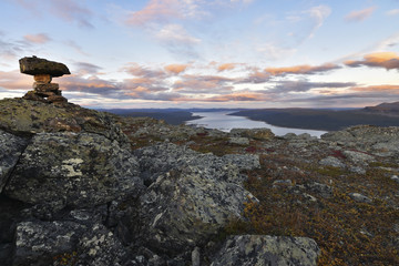 Fototapeta premium Pile of stones marks the mountain top, beautiful sunset and lake background
