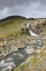 Waterfall lighted by sunlight in dramatic scene and dark clouds rolling in 