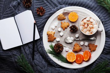 Christmas still life with hot cocoa, tangerines, cookies and empty notebook on knitted background from above. Delicious dessert for winter breakfast or brunch. Flat lay style.