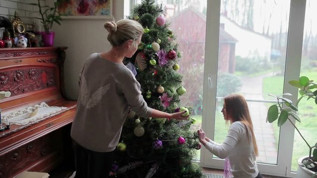 Two sisters decorating Christmas tree with a balls