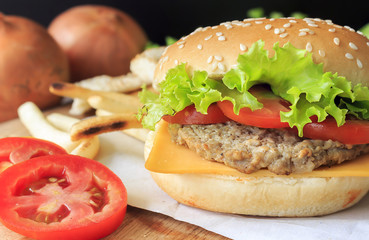 Grilled beef hamburger with vegetables on wood table, over light [blur and select focus background]