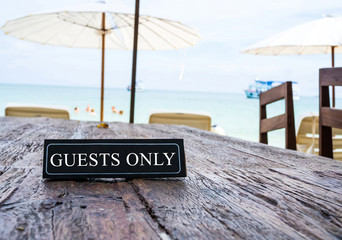 Guests only banner on restaurant table, beach background