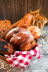 Different fresh bread in wicker basket on rustic table on wooden