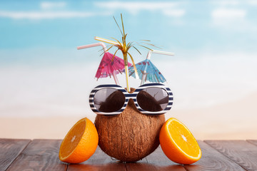 Coconut with straw, umbrellas, sunglasses and part orange against sea.