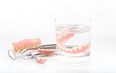 Close up of dentures in glass of water and dental hygienist mirr