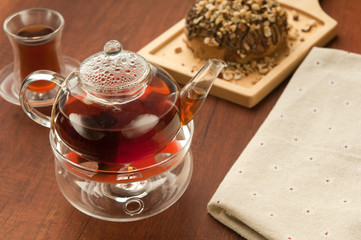 Transparent glass teapot and cup with tea on lerevyannoy surface brown and cookies on the board