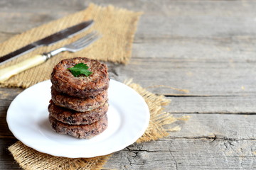Delicious bean burgers on a plate, fork, knife, burlap on old wooden background with copy space for text. Easy burgers cooked of boiled red beans chopped with a blender, garlic, eggs, flour and spices
