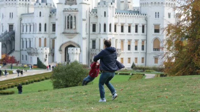 Father, spinning in circles his little son on a lawn in front of the Hluboka castle in Czech Republic