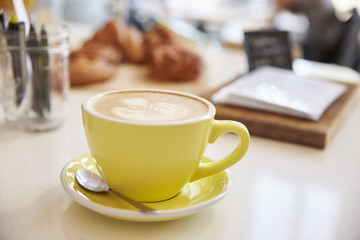 Large cappuccino coffee in yellow cup and saucer on counter