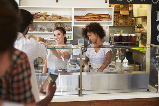 A queue of customers served by two women at a sandwich bar