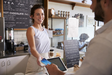 Customer at coffee shop pays smiling waitress with card