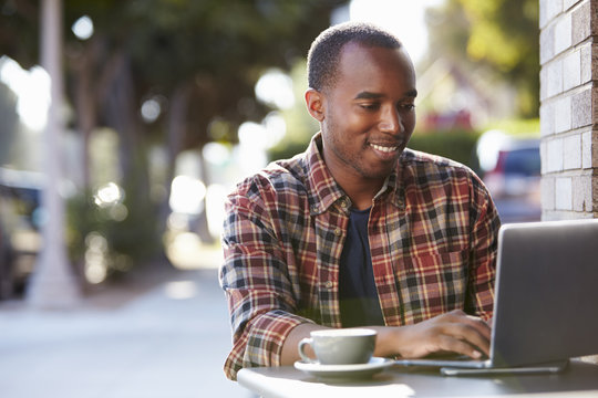 Young Black Man Using A Laptop Computer Outside A Cafe