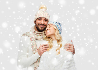 smiling couple in winter clothes hugging over snow