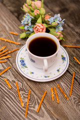 Small white cup of coffee, hazelnuts, cocoa beans, cookies and bouquet of flowers on wooden background