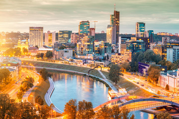 Fototapeta premium Cityscape view on the illuminated financial district with modern buildings, river and bridge during the sunset in Vilnius, Lithuania.