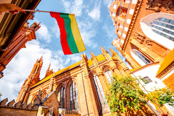View on the beautiful gothic saint Anna and Francis of Assisi churches eith lithuanian flag in the old town of Vilnius city, Lithuania. - obrazy, fototapety, plakaty