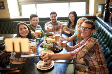 happy friends with selfie stick at bar or pub