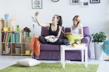 Two happy young female friends taking a selfie in the living room