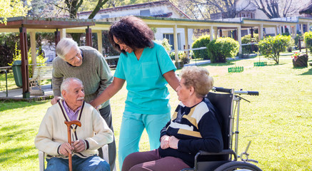 Afroamerican nurse joking with elder disabled people outdoor
