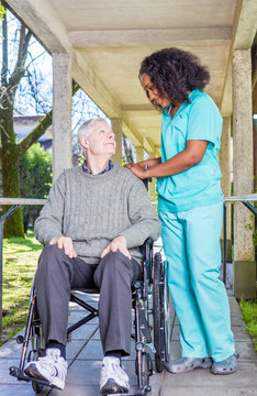Afroamerican nurse happy with caucasian elder patient on wheelch
