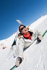 femme souriante avec des skis tombée par terre dans la neige