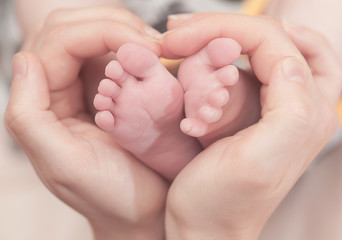 Obraz na płótnie Canvas Baby feet in mother hands. Feet on female heart shaped hands closeup. Happy family concept. Mom and her child.