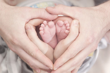 Children's feet in heartshaped hands of mother and father. Mother, father and Child. Happy Family concept. Beautiful conceptual image of Motherhood