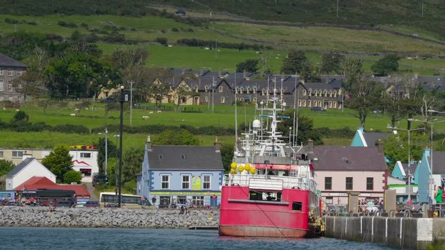 A big ferry on dock in the port of Dingle in Ireland where passengers are boarding the ship with the mountain on the background