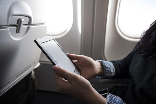 Woman sitting in airplane using E-Book, partial view