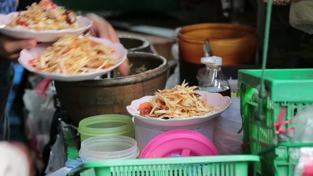 Female cook scooping SOMTUM, Green Papaya Salad, from mortar and putting into dishes and serving.

