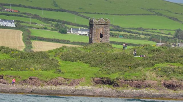 A small tower in the hill and small boat the small tower ruins on a hill with some people taking photos that is found in a village in Ireland