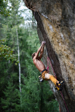 Male rock climber struggles to reach his next grip on a steep cliff. Extreme sport.