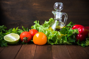 Fresh tomatoes, lime, sweet pepper, lettuce, parsley and olive oil on dark wood background. Healthy food. Vegetables and greens. Salad ingredients.