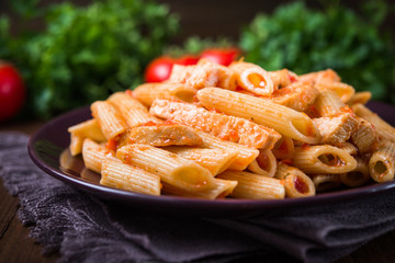 Penne pasta with chicken and tomato sauce on dark wooden background close up. Italian cuisine.