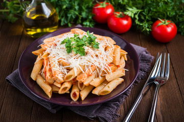 Penne pasta with chicken, tomato sauce, parmesan cheese and parsley on dark wooden background close...